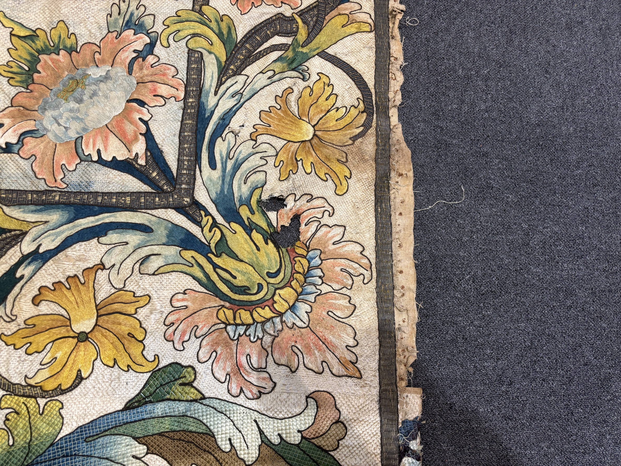 A large early 18th century possibly French polychrome and gold metallic silk embroidered wall hanging, with scrolling vine and floral border. The central motifs embroidered with an elaborate metallic thread cartouche fra